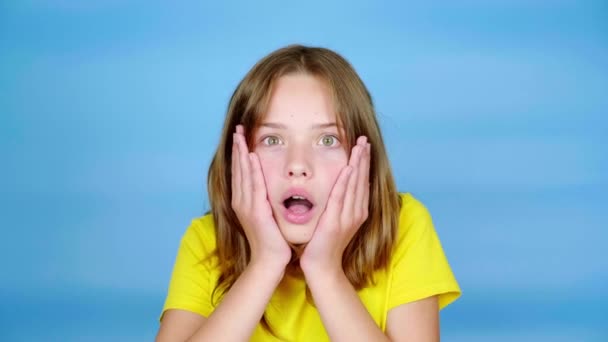 穿着黄色T恤的少女把手放在头上 张大了嘴 非常吃惊 蓝色背景 有复制空间 青少年的情绪 4K镜头 — 图库视频影像