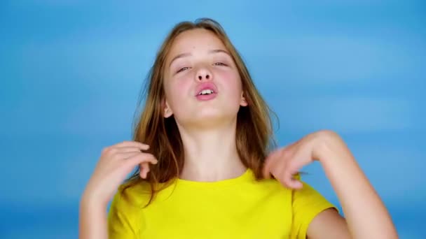 穿着黄色T恤的少女正在理直头发和说话 她解释道 蓝色背景 有复制空间 青少年的情绪 4K镜头 — 图库视频影像