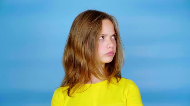 黄色のTシャツを着た10代の女の子がテキストの場所を見て 何を選択するかを考えています コピースペース付きの青の背景 10代の感情4K映像 — ストック動画
