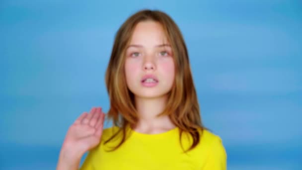 穿着黄色T恤的少女看着摄像机 把手伸到前面说 蓝色背景 有复制空间 集中在手上 青少年的情绪 4K镜头 — 图库视频影像