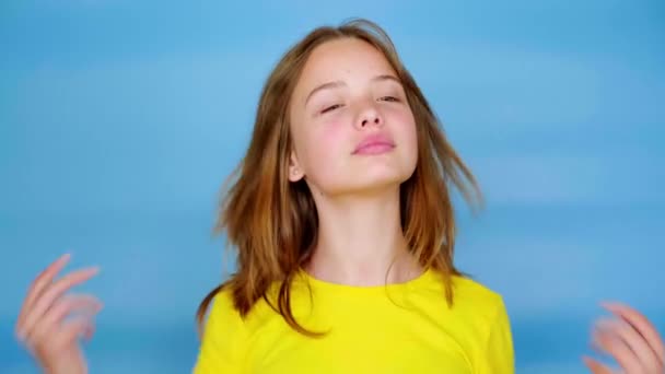 黄色のTシャツの10代の女の子は彼女の髪と笑顔をまっすぐにしています コピースペース付きの青の背景 10代の感情4K映像 — ストック動画