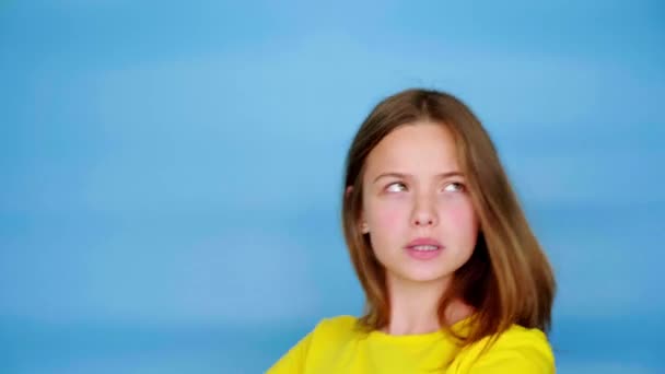 Gelukkig Tienermeisje Een Geel Shirt Danst Glimlacht Rotzooit Blauwe Achtergrond — Stockvideo