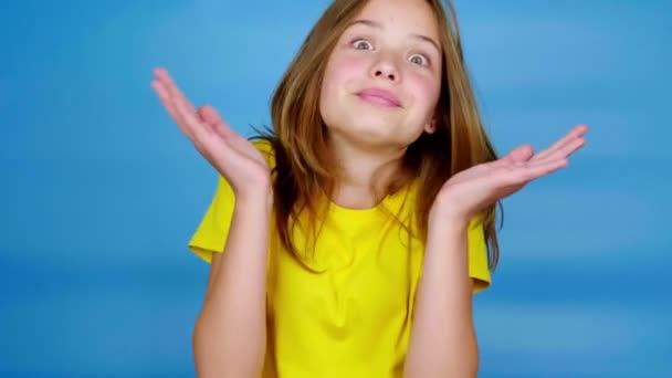 穿着黄色T恤的少女耸了耸肩 回头看着镜头 不知道是怎么回事 蓝色背景 有复制空间 青少年的情绪 4K镜头 — 图库视频影像