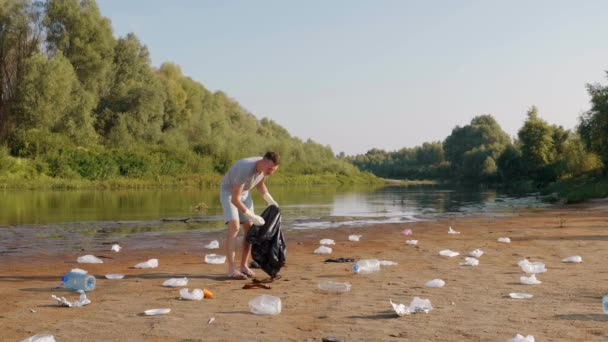 Człowiek zbiera plastikowe śmieci na brzegach suchej i zanieczyszczonej rzeki lub jeziora — Wideo stockowe