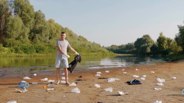 De mens staat tussen afval en danst de flosdraad op de oevers van de droge en vervuilde rivier — Stockvideo