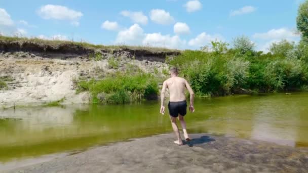 Un jeune homme court et plonge dans une rivière sèche et polluée . — Video