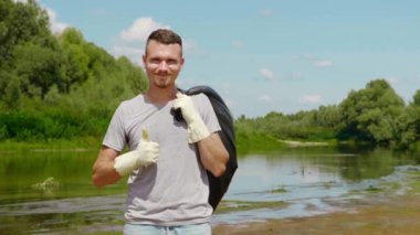 Adam plastik bir torbayla ayakta duruyor ve baş parmağını kaldırıyor..
