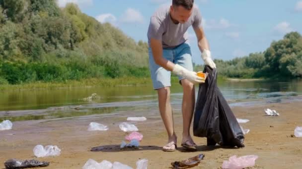 A man is collects plastic trash on the banks of a dry and polluted river or lake — 비디오