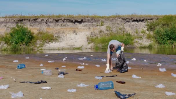 Un uomo raccoglie rifiuti di plastica sulle rive di un fiume o di un lago secco e inquinato — Video Stock