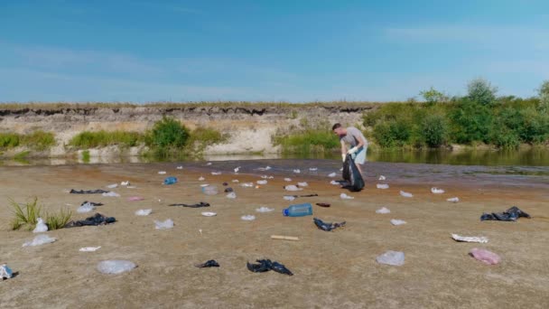 Ein Mann sammelt Plastikmüll am Ufer eines trockenen und verschmutzten Flusses oder Sees — Stockvideo