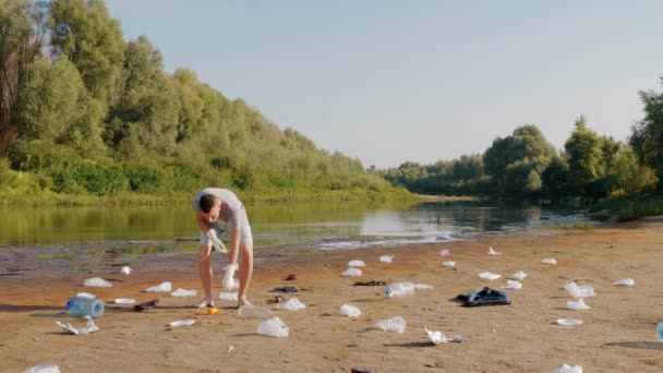 Чоловік підбирає пластикові сміття на берегах забрудненої річки і показує свою неприязнь . — стокове відео