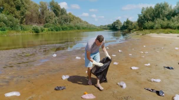 Homem é coleta de lixo plástico nas margens de um rio ou lago seco e poluído . — Vídeo de Stock