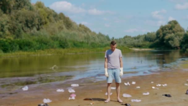 Man stands along plastic trash on the banks of polluted river and shows dislike — 비디오