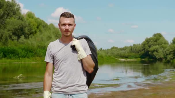男は乾燥した汚染された川の岸に背中の後ろにビニール袋で立っている — ストック動画