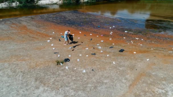 Vista aérea do homem que coleta lixo plástico nas margens do rio poluído — Vídeo de Stock