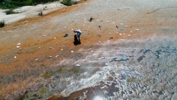 Vista aérea do homem que coleta lixo plástico nas margens do rio poluído — Vídeo de Stock