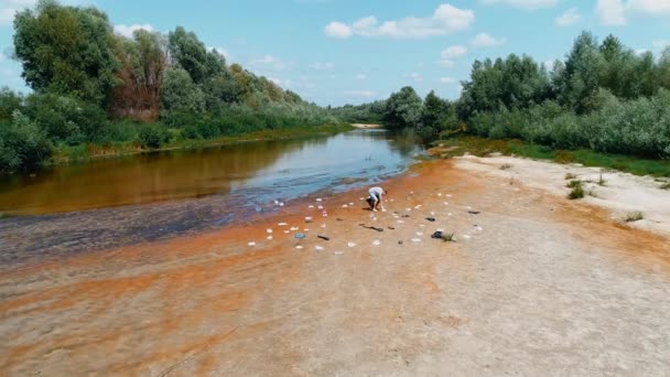 Kirlenmiş nehrin kıyısında plastik çöpleri toplayan adamın havadan görünüşü — Stok video