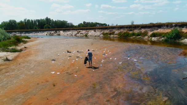 Vista aérea del hombre que recoge basura plástica en las orillas del río contaminado — Vídeos de Stock