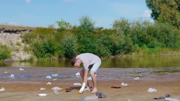 Człowiek zbiera plastikowe śmieci na brzegach zanieczyszczonej rzeki, pokazuje, że nie lubi. — Wideo stockowe