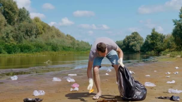 Человек собирает пластиковый мусор на берегу сухой и загрязненной реки — стоковое видео