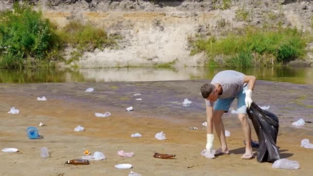 Man collects plastic trash on the banks of a dry and polluted river or lake — Stock Video