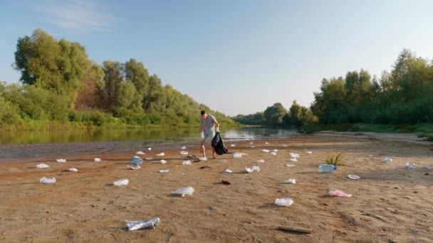 Hombre bailando y recoge basura plástica en las orillas del río contaminado — Vídeos de Stock