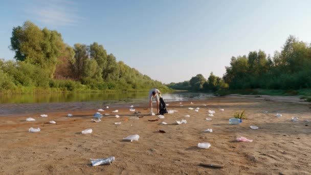 Ο άνθρωπος χορεύει και μαζεύει πλαστικά σκουπίδια στις όχθες του μολυσμένου ποταμού. — Αρχείο Βίντεο