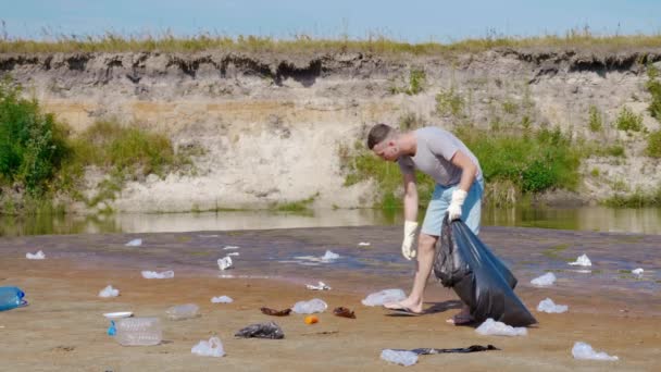 Man collects plastic trash on the banks of a dry and polluted river — Stock Video