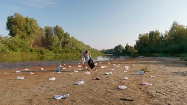 Ο άνθρωπος συλλέγει πλαστικά σκουπίδια στις όχθες του μολυσμένου ποταμού και δείχνει αντίχειρες προς τα πάνω. — Αρχείο Βίντεο