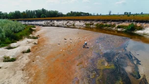 Vue aérienne de l'homme qui ramasse les déchets plastiques sur les rives d'une rivière sèche et polluée — Video