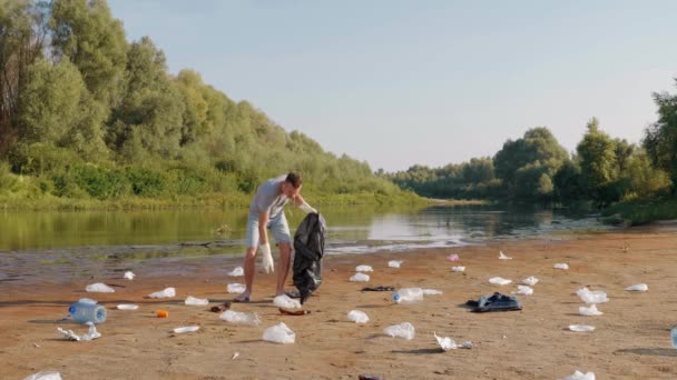 Homem dançando e coleta lixo plástico nas margens do rio poluído — Vídeo de Stock