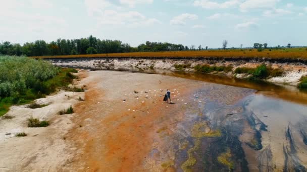 Vista aérea del hombre que recoge basura plástica en las orillas del río contaminado — Vídeos de Stock