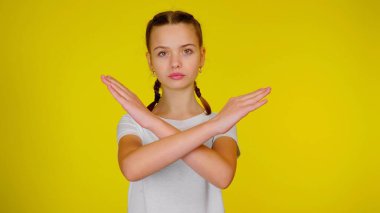 Teen girl in a white t-shirt keeps her arms crossed on yellow background