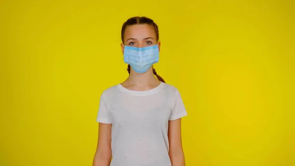Tini lány orvosi maszk néz kamera sárga háttér — Stock Fotó