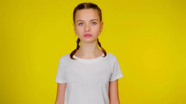 Teen girl in a white t-shirt looking at the camera on yellow background — 스톡 사진