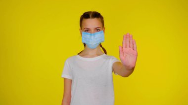 Teen girl in medical mask holds her hand in a front on yellow background