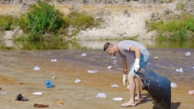 İnsan dans ediyor ve kirlenmiş nehir kıyısında plastik çöpleri topluyor.