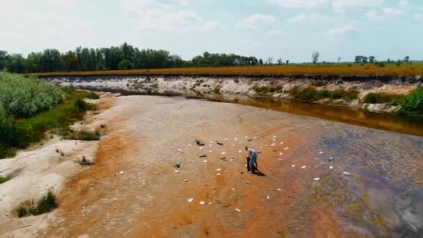 Вид с воздуха на человека, который собирает пластиковый мусор на берегу загрязненной реки — стоковое видео
