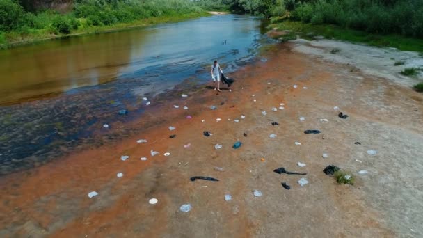 Luftaufnahme eines Mannes, der Plastikmüll am Ufer des verschmutzten Flusses sammelt — Stockvideo