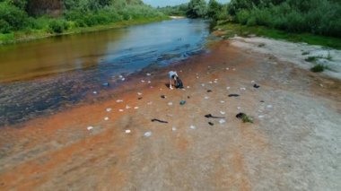 Kirlenmiş nehrin kıyısında plastik çöpleri toplayan adamın havadan görünüşü