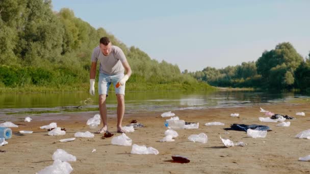 L'uomo raccoglie rifiuti di plastica sulle rive del fiume inquinato e mostra antipatia — Video Stock