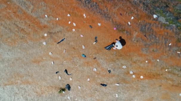 Vue aérienne du dessus de l'homme qui ramasse les déchets plastiques sur les rives d'une rivière polluée — Video