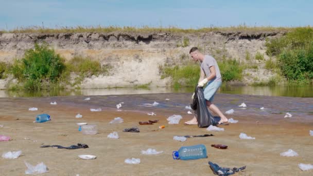 Hombre bailando y recoge basura plástica en las orillas del río contaminado — Vídeos de Stock