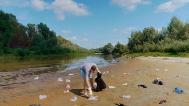 怒りの男は汚染された川のほとりにプラスチックごみを収集し、その後ゴミを落とす — ストック動画