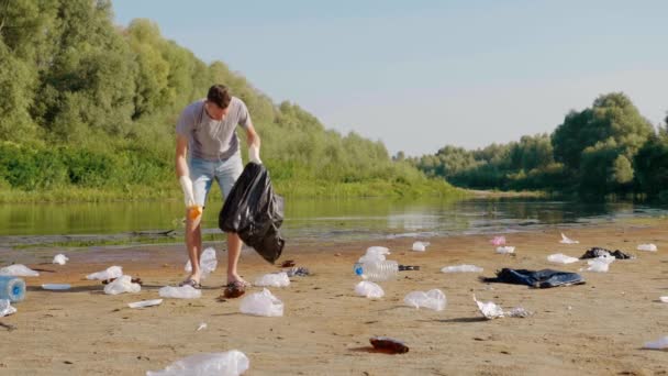 Man verzamelt plastic afval op oevers van vervuilde rivier en toont duimen omhoog — Stockvideo