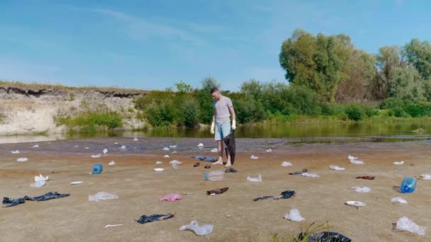 Muž sbírá plastové odpadky na březích znečištěné řeky — Stock video