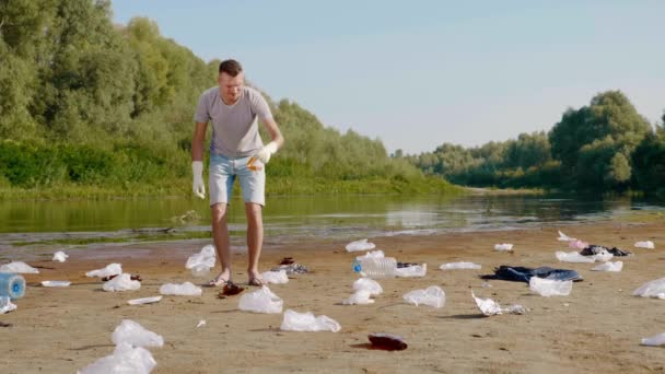 L'uomo raccoglie rifiuti di plastica sulle rive del fiume inquinato e mostra antipatia — Video Stock