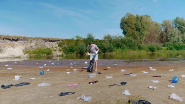 El hombre recoge basura plástica en las orillas del río contaminado y muestra los pulgares hacia arriba — Vídeo de stock