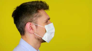 Young man in a medical mask stands in profile on yellow background