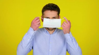 Young man puts on a medical mask on yellow background with copy space.